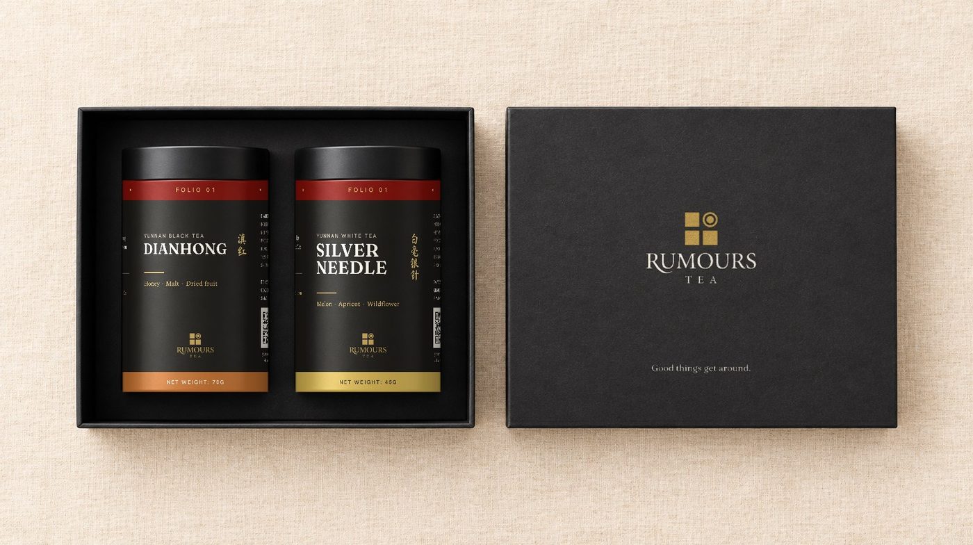 The gift box open, a Dianhong tin and a Silver Needle tin lying side by side, the lid beside it with the Rumours Tea logo